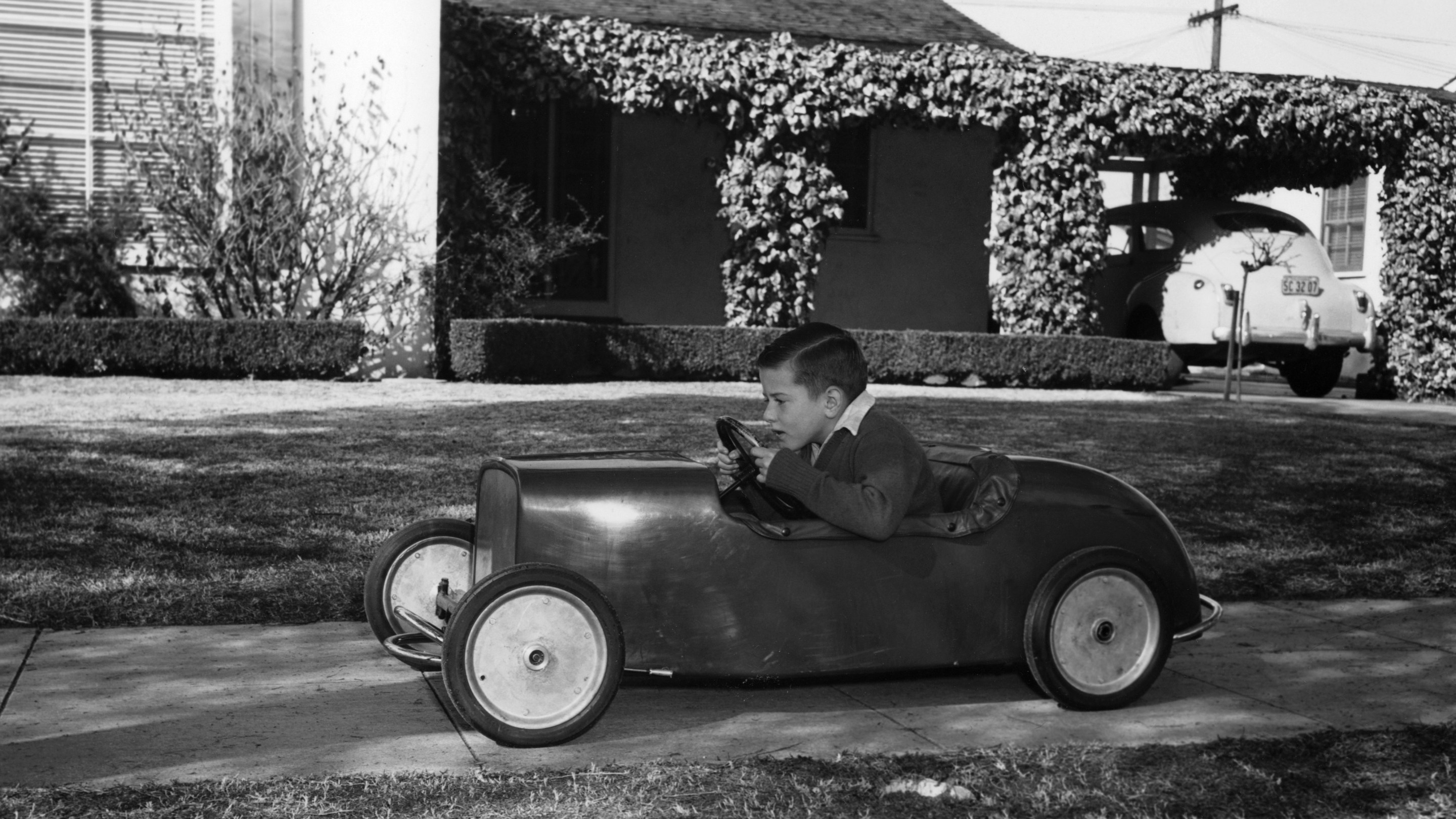 Boy in a pedal car. Driving his pedal car on the pavement outside his house.
