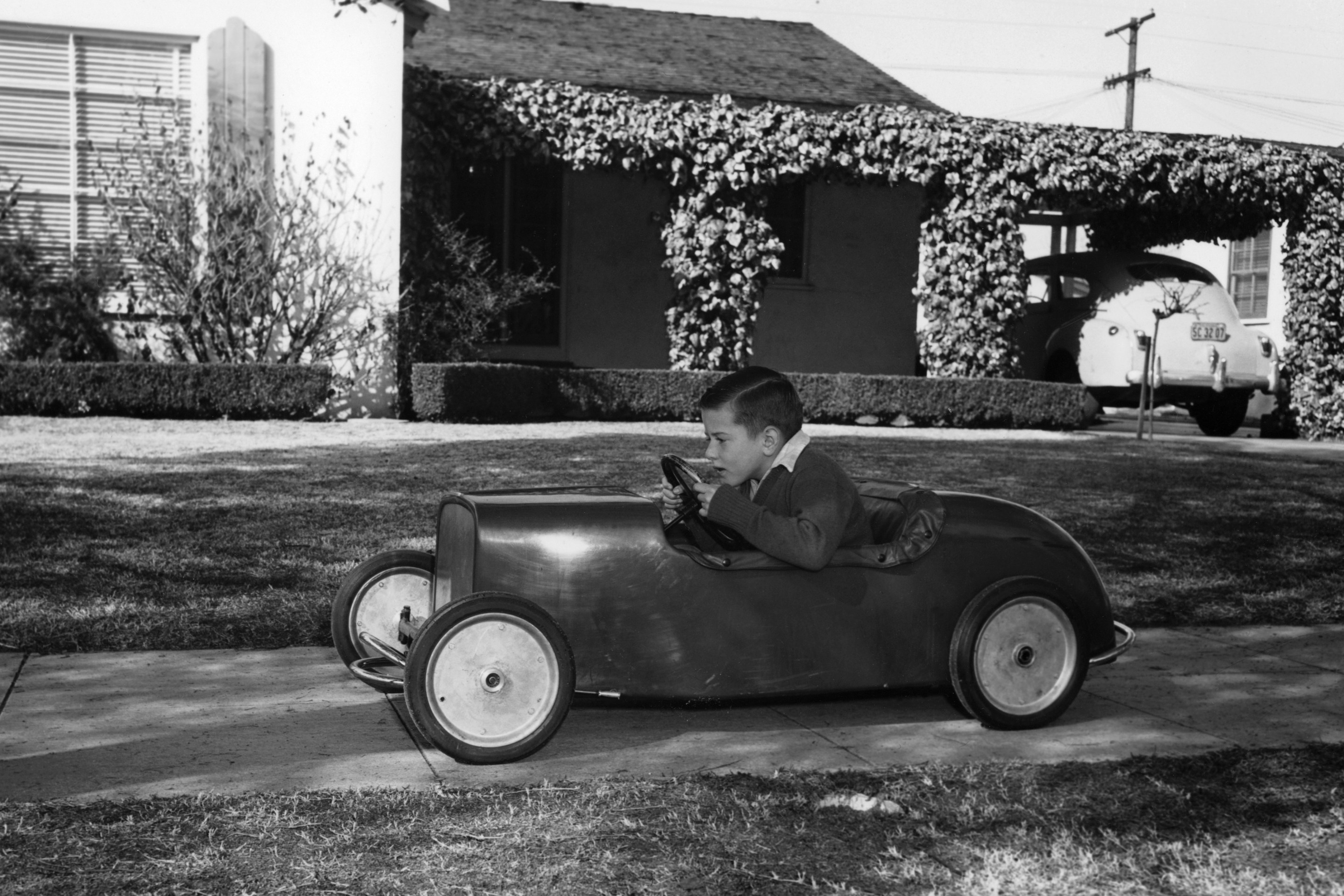 Boy in a pedal car. Driving his pedal car on the pavement outside his house.