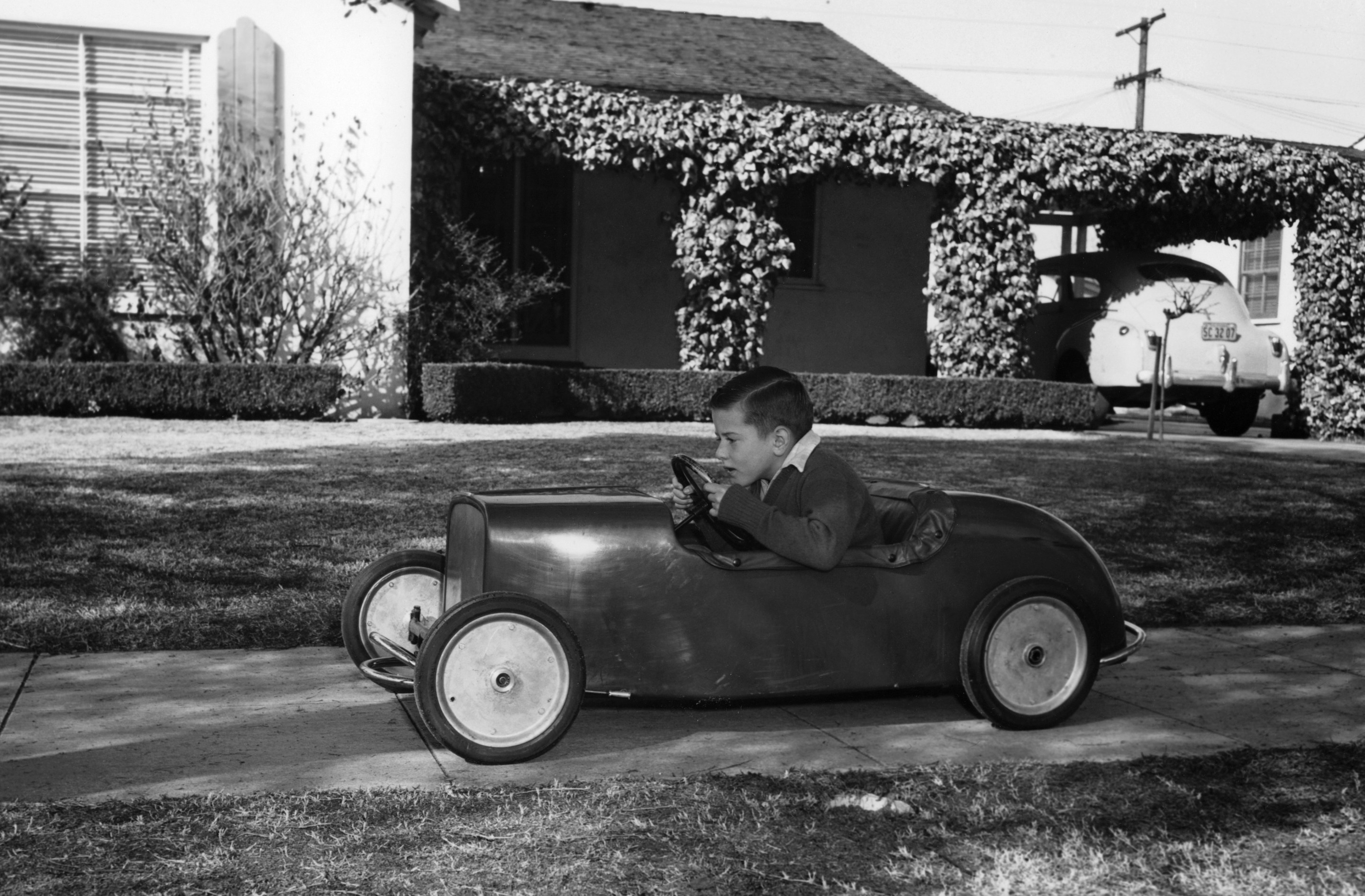 Boy in a pedal car. Driving his pedal car on the pavement outside his house.