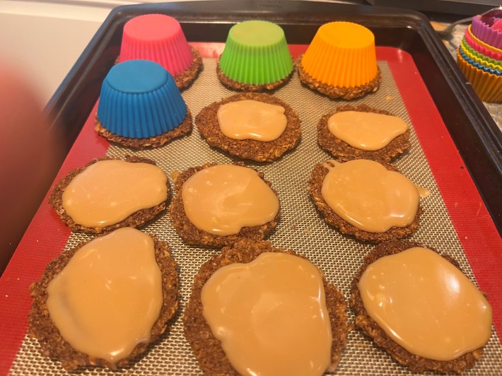 Silicone muffin cups dump out liquid caramel onto baked cookies.
