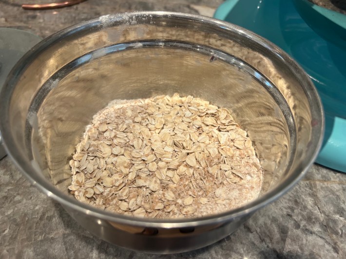 Oats, flour, bran meal, and baking soda, in a metal bowl.