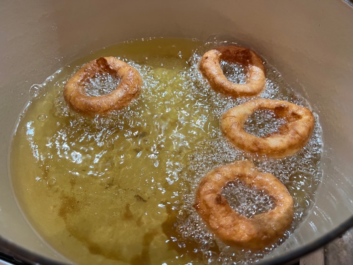 Four donut rings fry in hot oil.