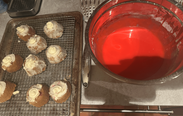 Small cakes on the right next to a vat of red icing.