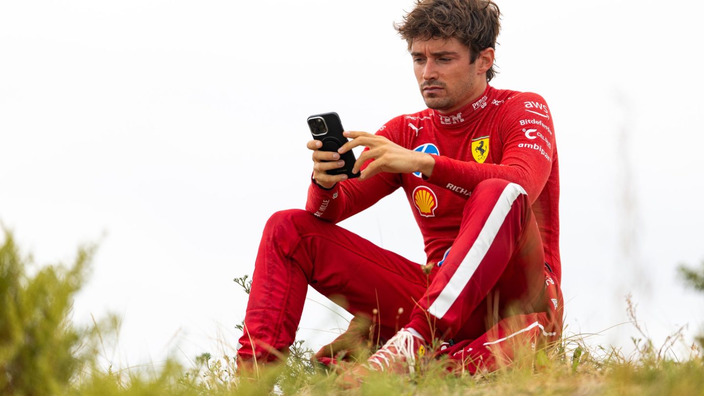 Charles Leclerc of Monaco and Ferrari uses his phone on the embankment following his crash.