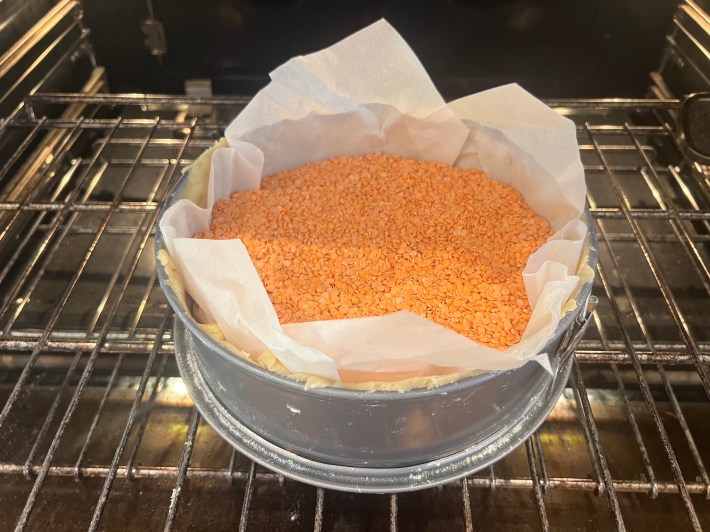 Lentils are used as baking beans inside a tart pan, inside an oven.