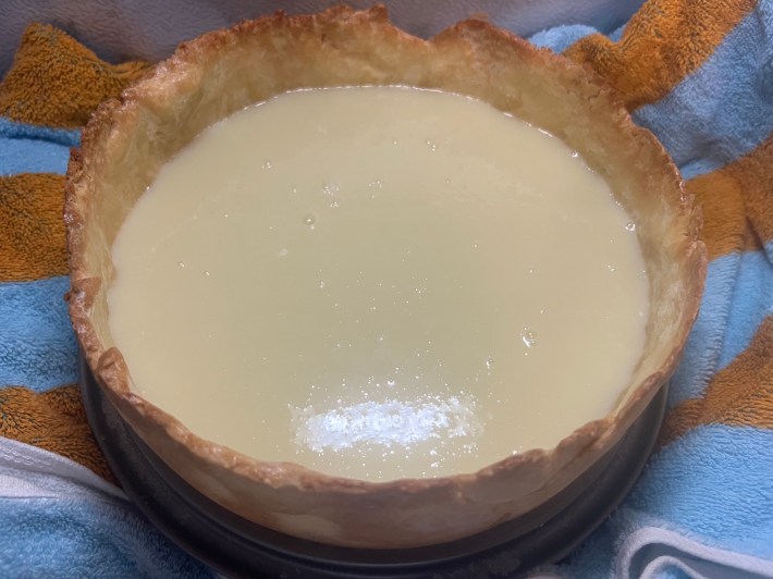 White chocolate ganache poured into a tart crust, resting on a towel inside a freezer