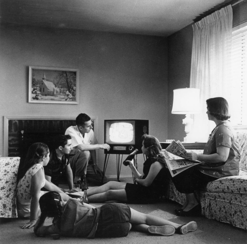 A black and white photo of a family gathered around a 1950s era television.