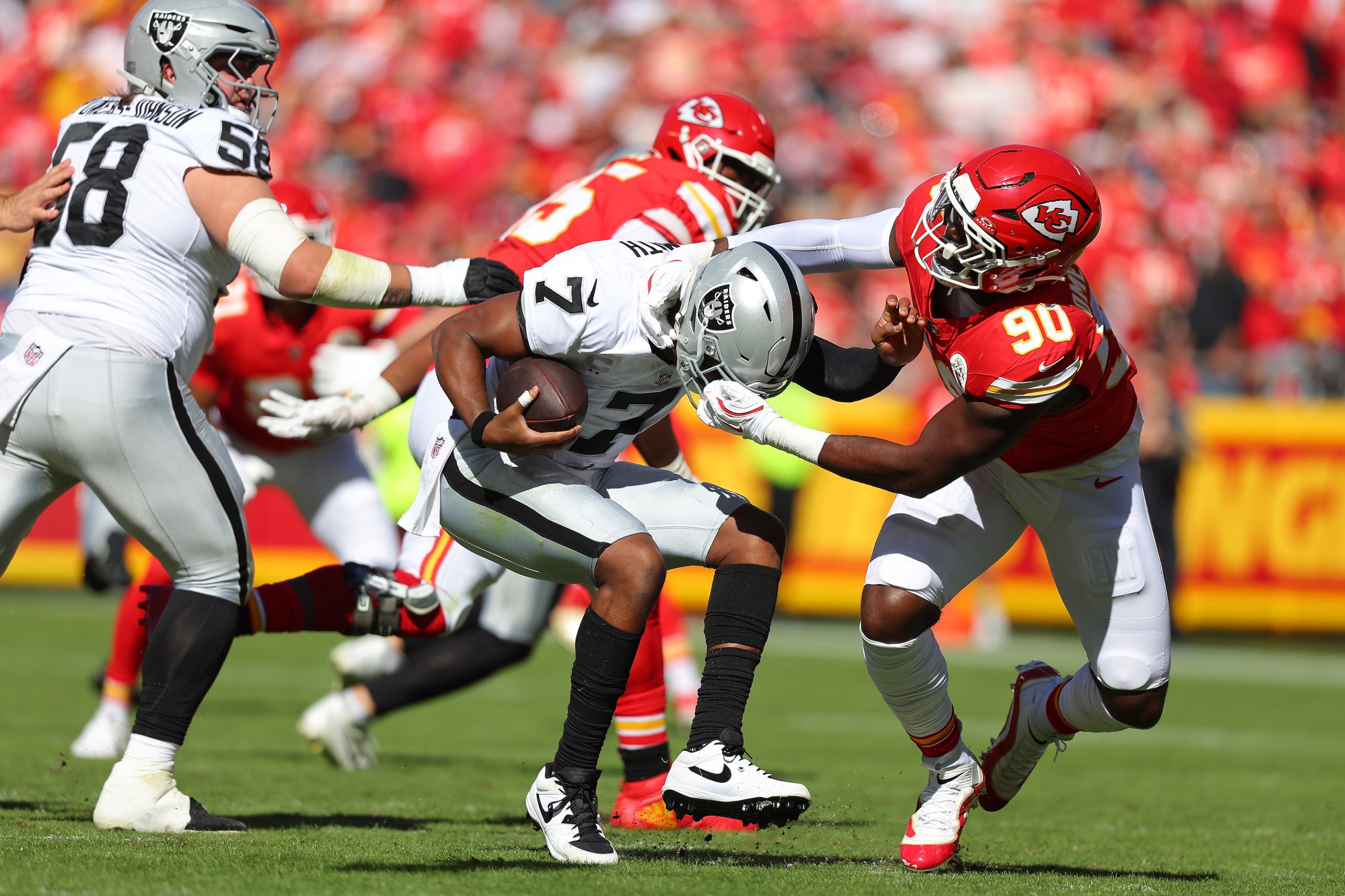 Charles Omenihu #90 of the Kansas City Chiefs grabs the face mask of Geno Smith #7 of the Las Vegas Raiders during the first quarter in the game at Arrowhead Stadium on October 19, 2025 in Kansas City, Missouri.