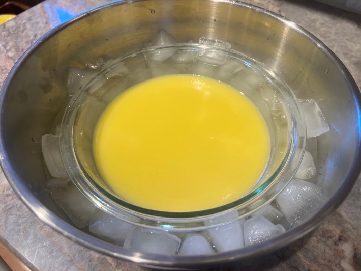 Warm lemon curd in a glass bowl, resting in an ice bath