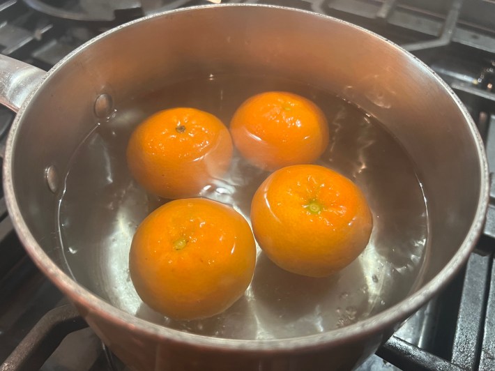 Four clementines float in simmering water.