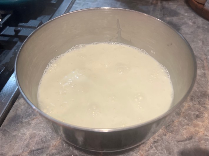 Hot cream poured over white chocolate chips in a metal bowl