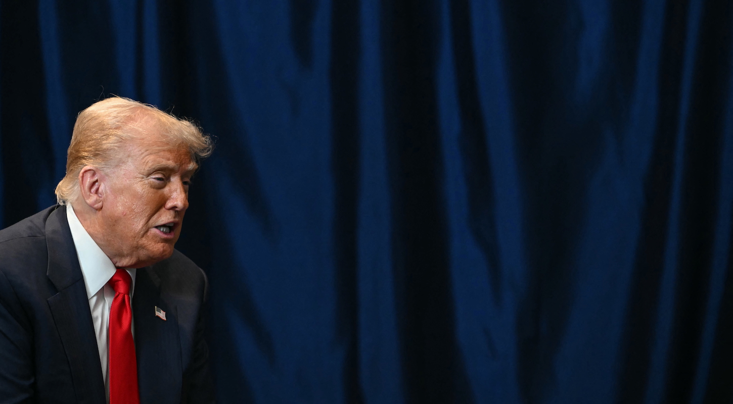 Donald Trump, looking like shit in front of a blue curtain.