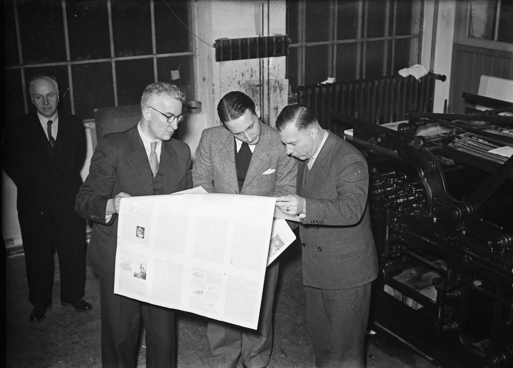 Three men bend over a newspaper just off the printing press, January 7, 1947, assignments, The Netherlands, 20th century press agency photo, news to remember, documentary, historic photography 1945-1990, visual stories, human history of the Twentieth Century, capturing moments in time.