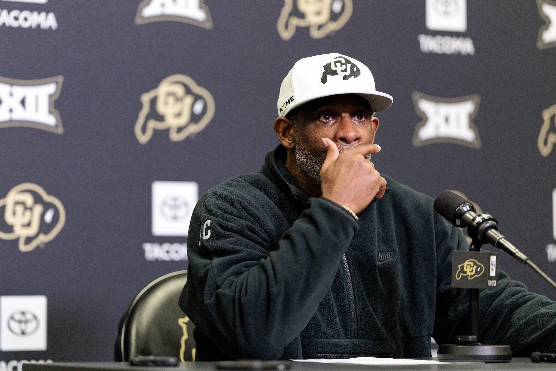 Deion Sanders sitting at a table during a press conference.
