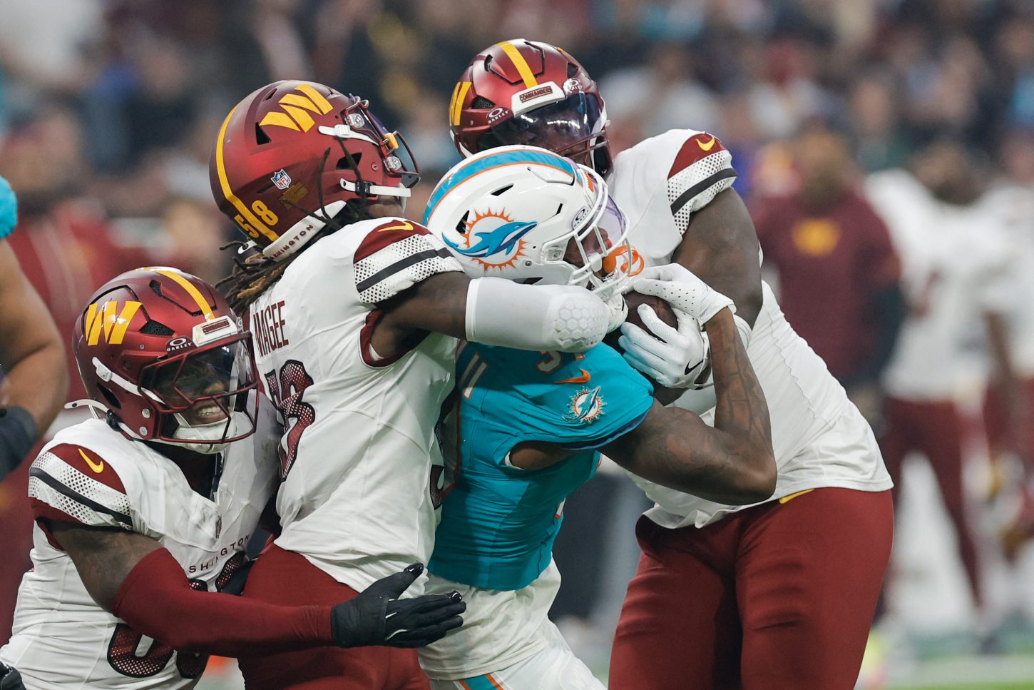 A bunch of Washington Commanders tackle a Miami Dolphin.