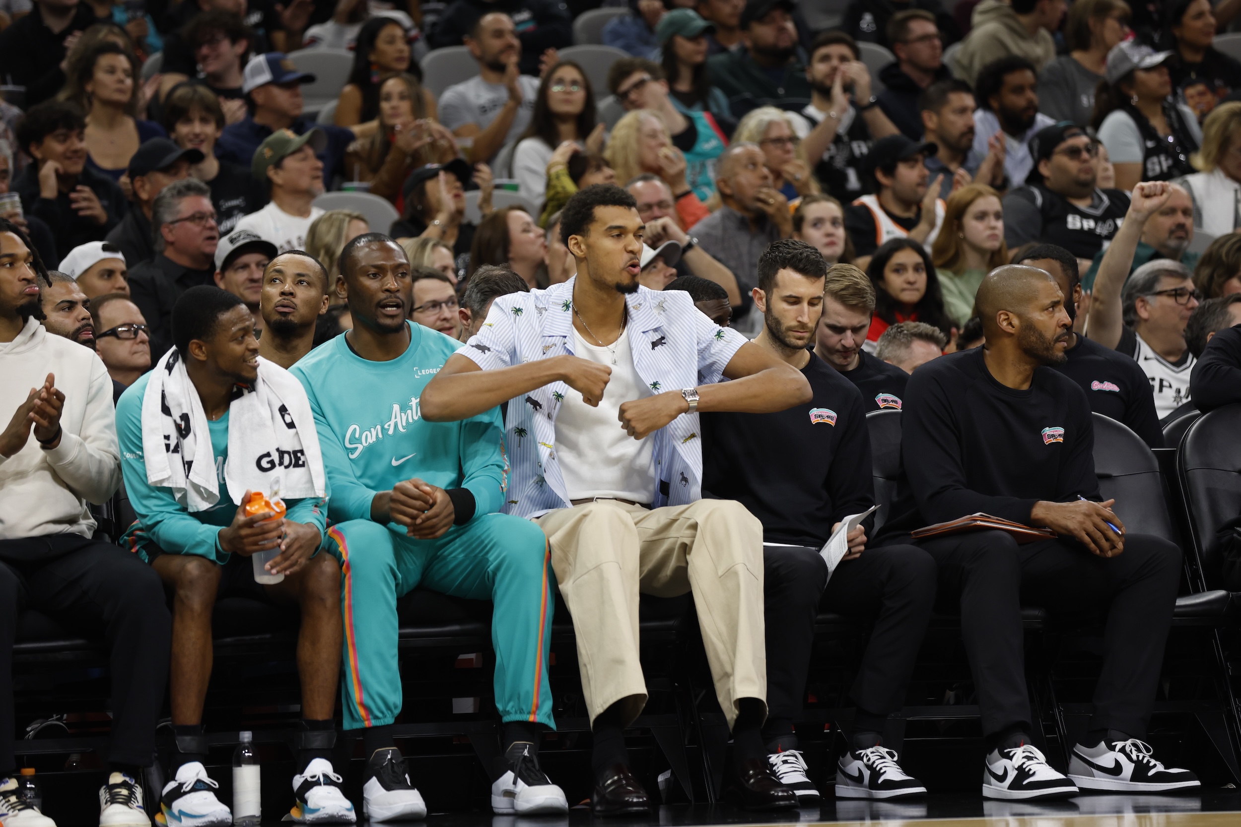 Victor Wembanyama sits court-side in street clothes.
