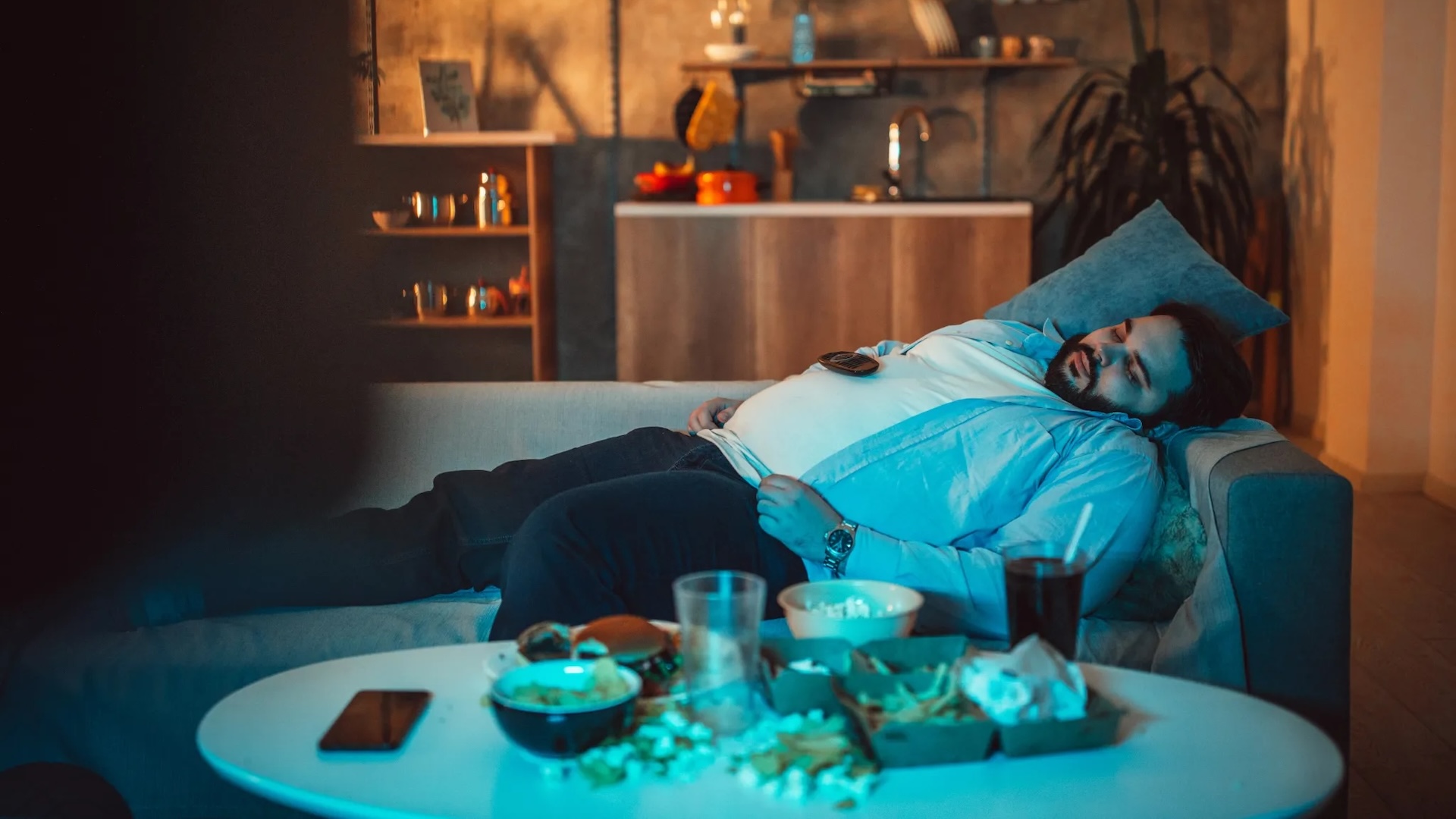 A man is asleep on a couch in front of a television.