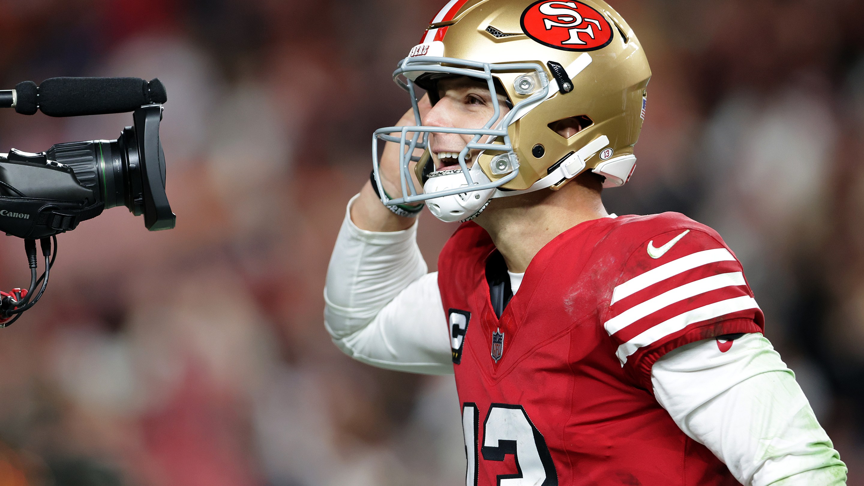 San Francisco 49ers' Brock Purdy celebrates his 2nd quarter rushing touchdown against Chicago Bears on December 28, 2025. He's doing the cupped-ear "let me hear it" gesture into a TV camera's lens.