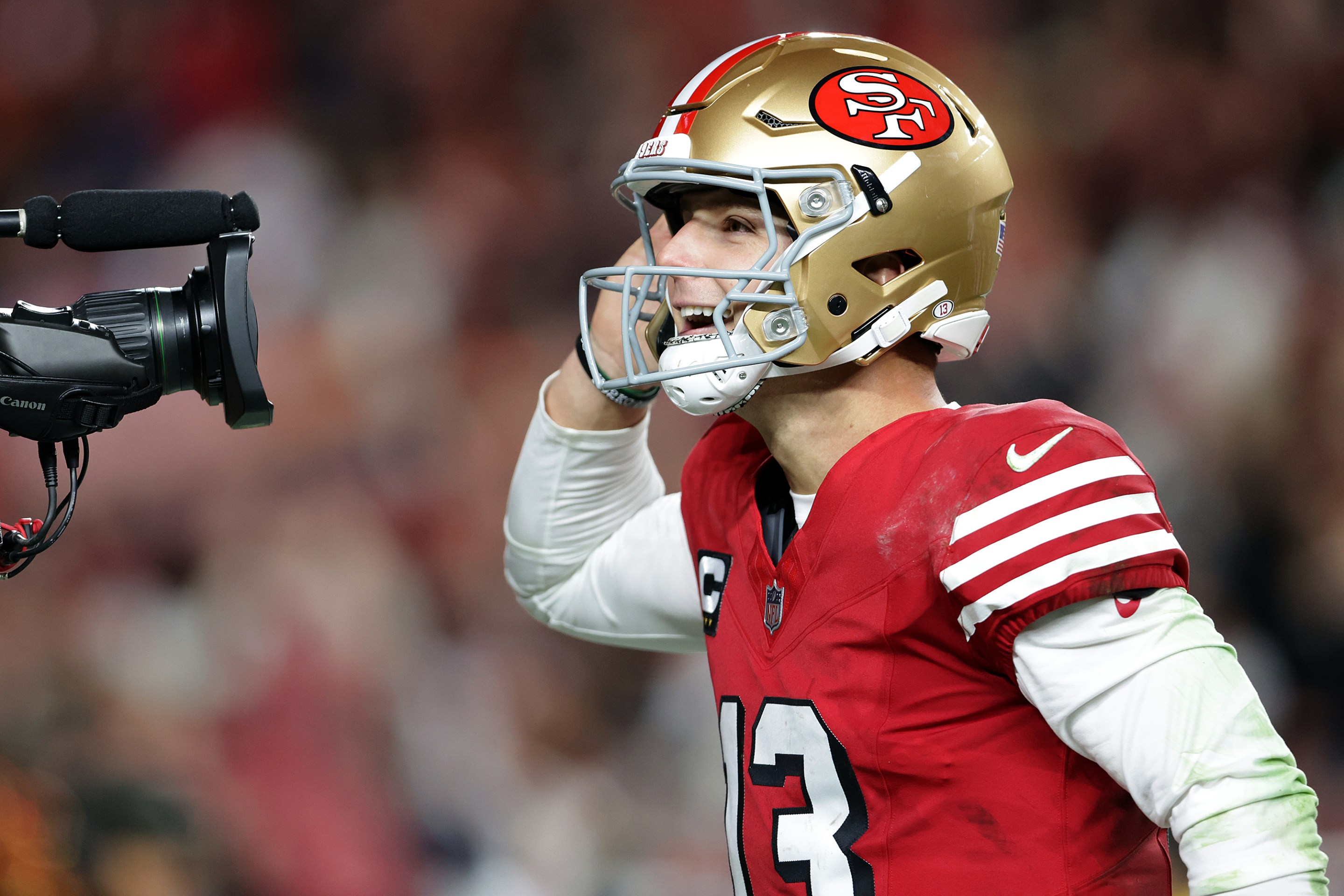 San Francisco 49ers' Brock Purdy celebrates his 2nd quarter rushing touchdown against Chicago Bears on December 28, 2025. He's doing the cupped-ear "let me hear it" gesture into a TV camera's lens.