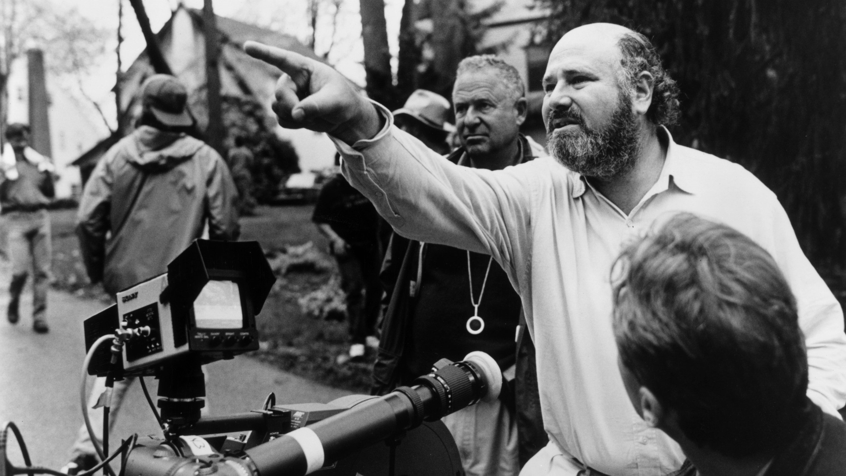 American director, producer, and actor Rob Reiner gestures near a camera while crew members surround him outdoors on the set of his film, 'North.'