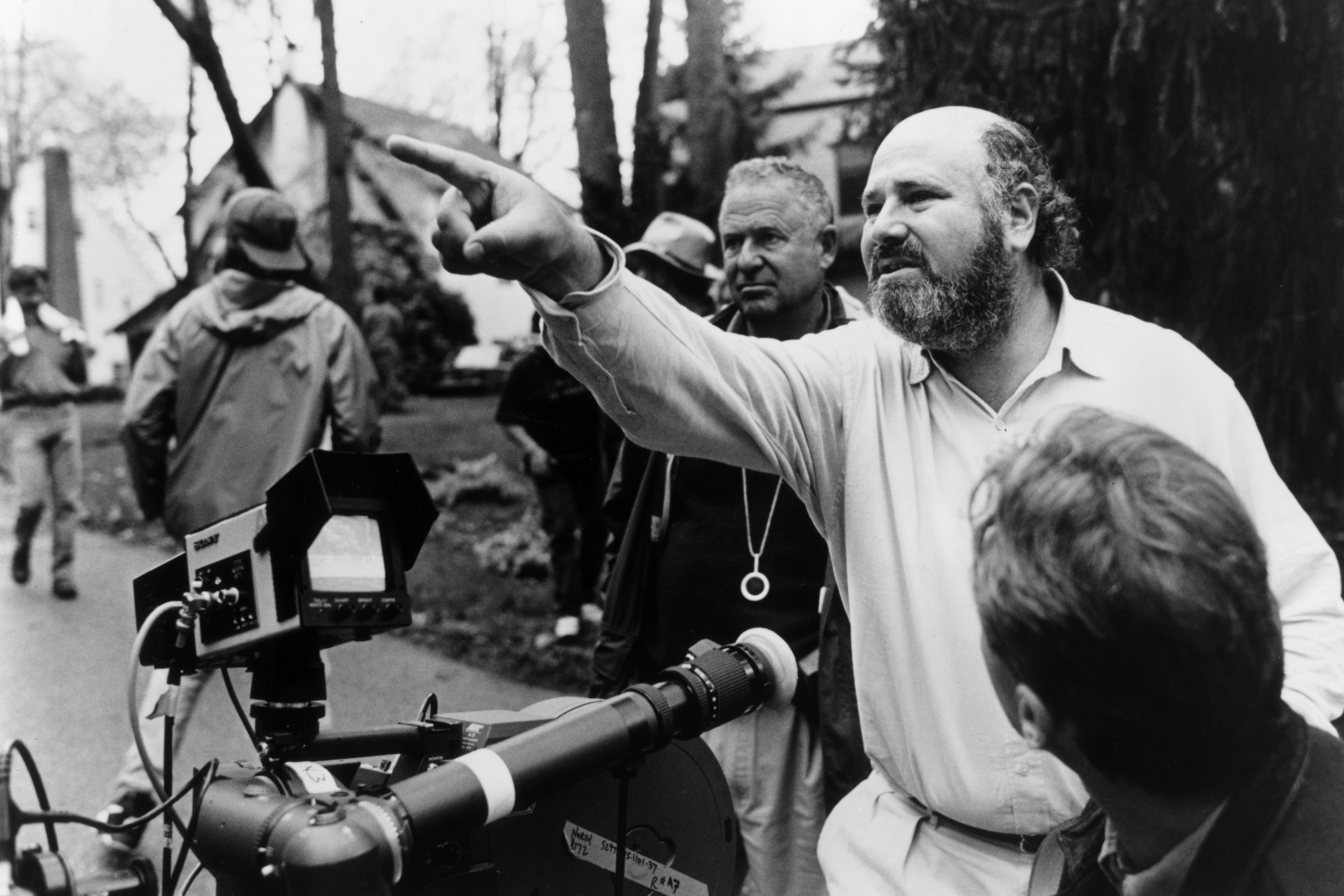 American director, producer, and actor Rob Reiner gestures near a camera while crew members surround him outdoors on the set of his film, 'North.'