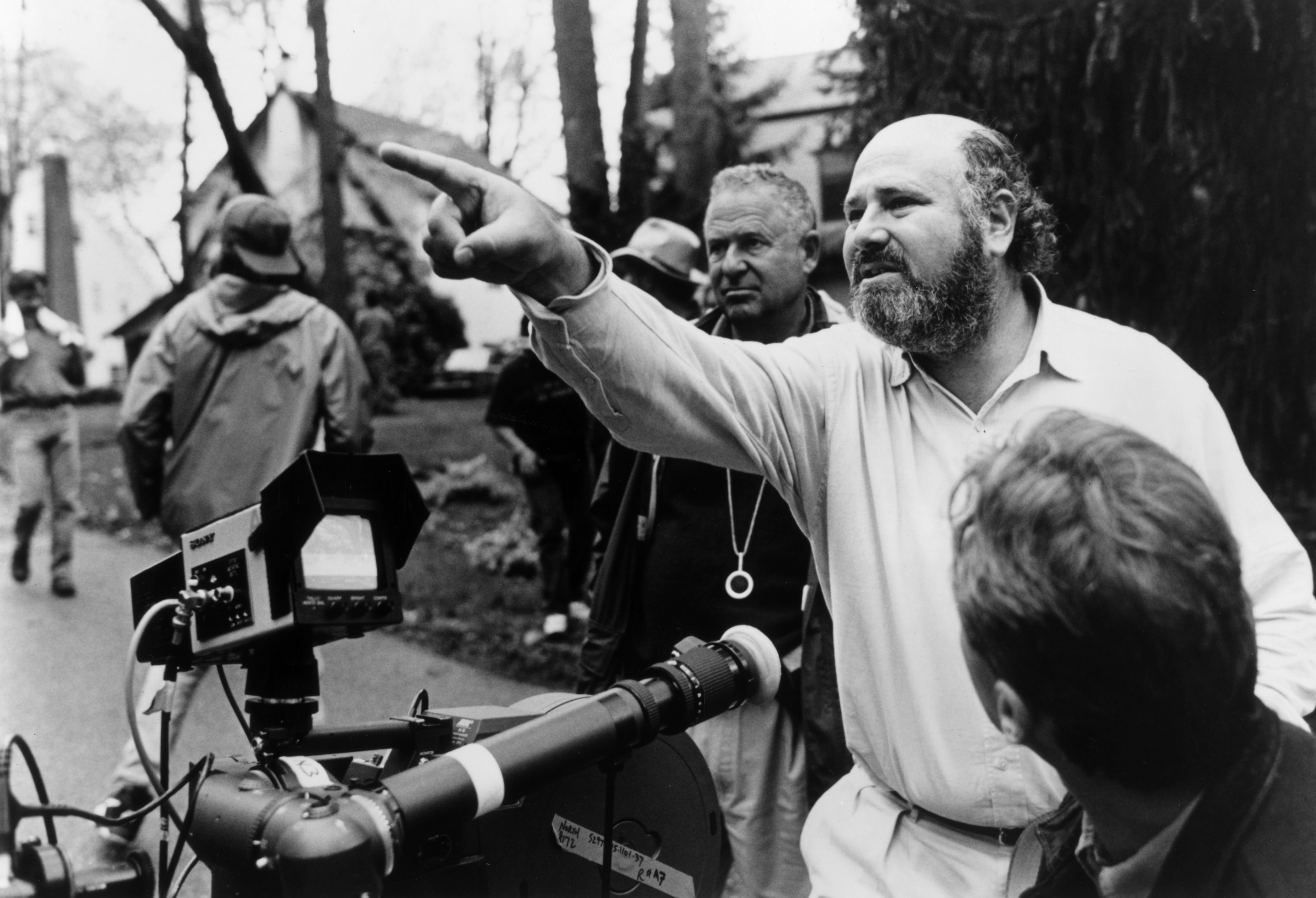 American director, producer, and actor Rob Reiner gestures near a camera while crew members surround him outdoors on the set of his film, 'North.'