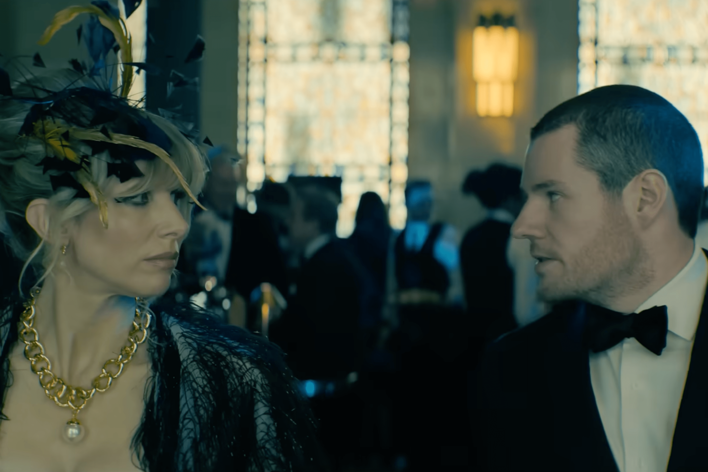 a still from the movie Jingle Bell Heist, with Lucy Punch in a fascinator looking at Connor Swindells