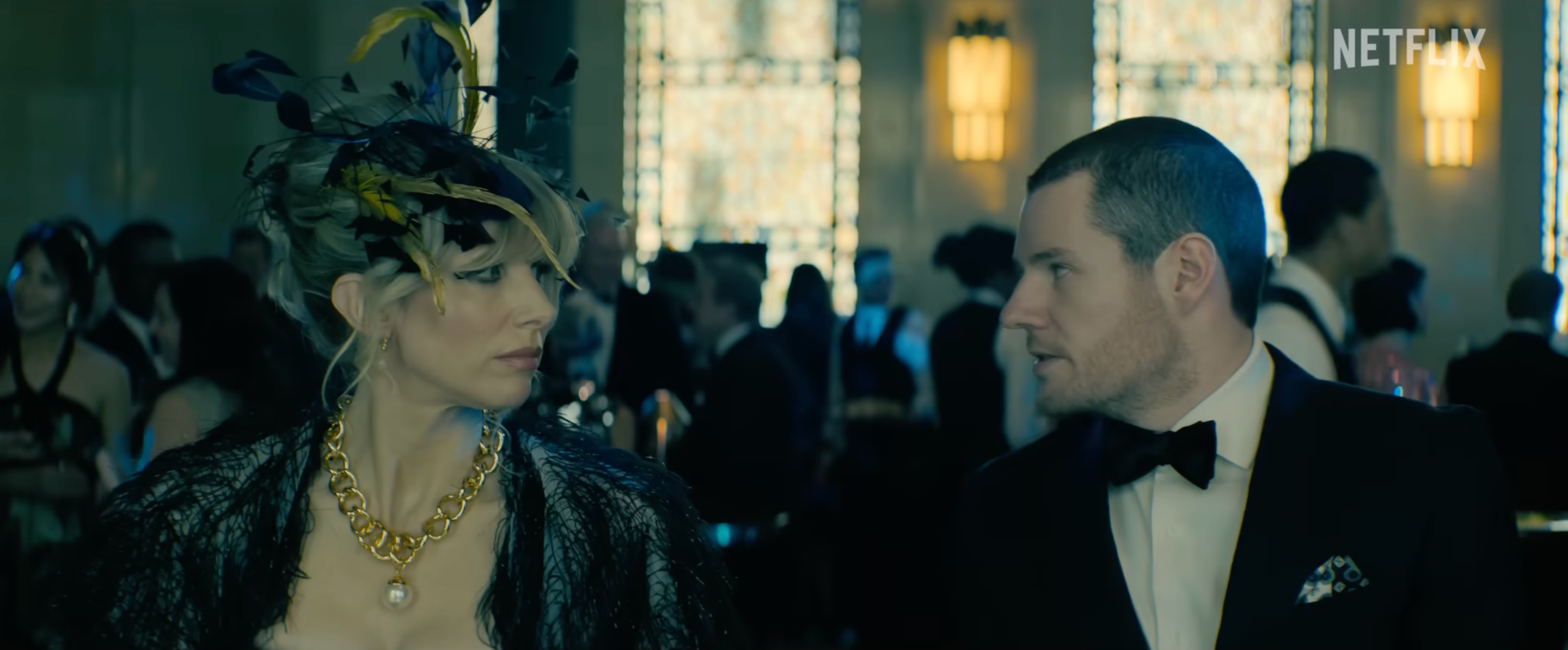 a still from the movie Jingle Bell Heist, with Lucy Punch in a fascinator looking at Connor Swindells