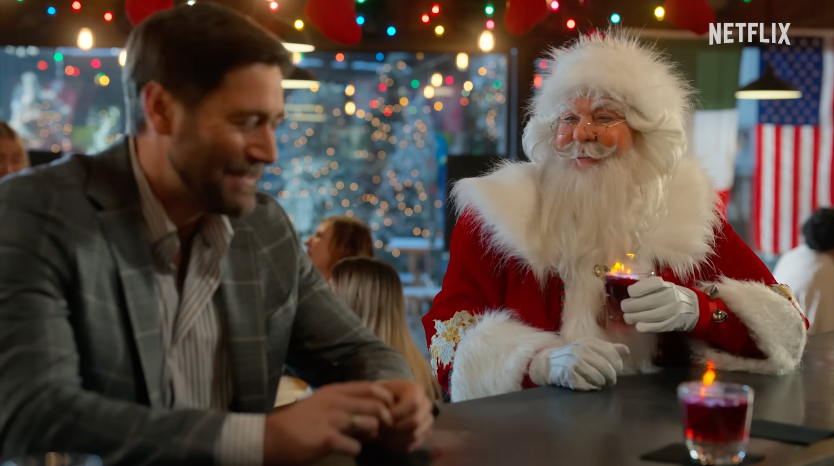 a photo of a woman dressed in drag as Santa Claus holding a flaming shot glass looking at a blurry man