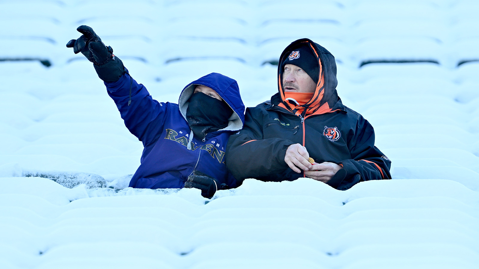 A Baltimore Ravens and Cincinnati Bengals fan are seen prior to a game at Paycor Stadium on December 14, 2025 in Cincinnati, Ohio. There is snow all around them.