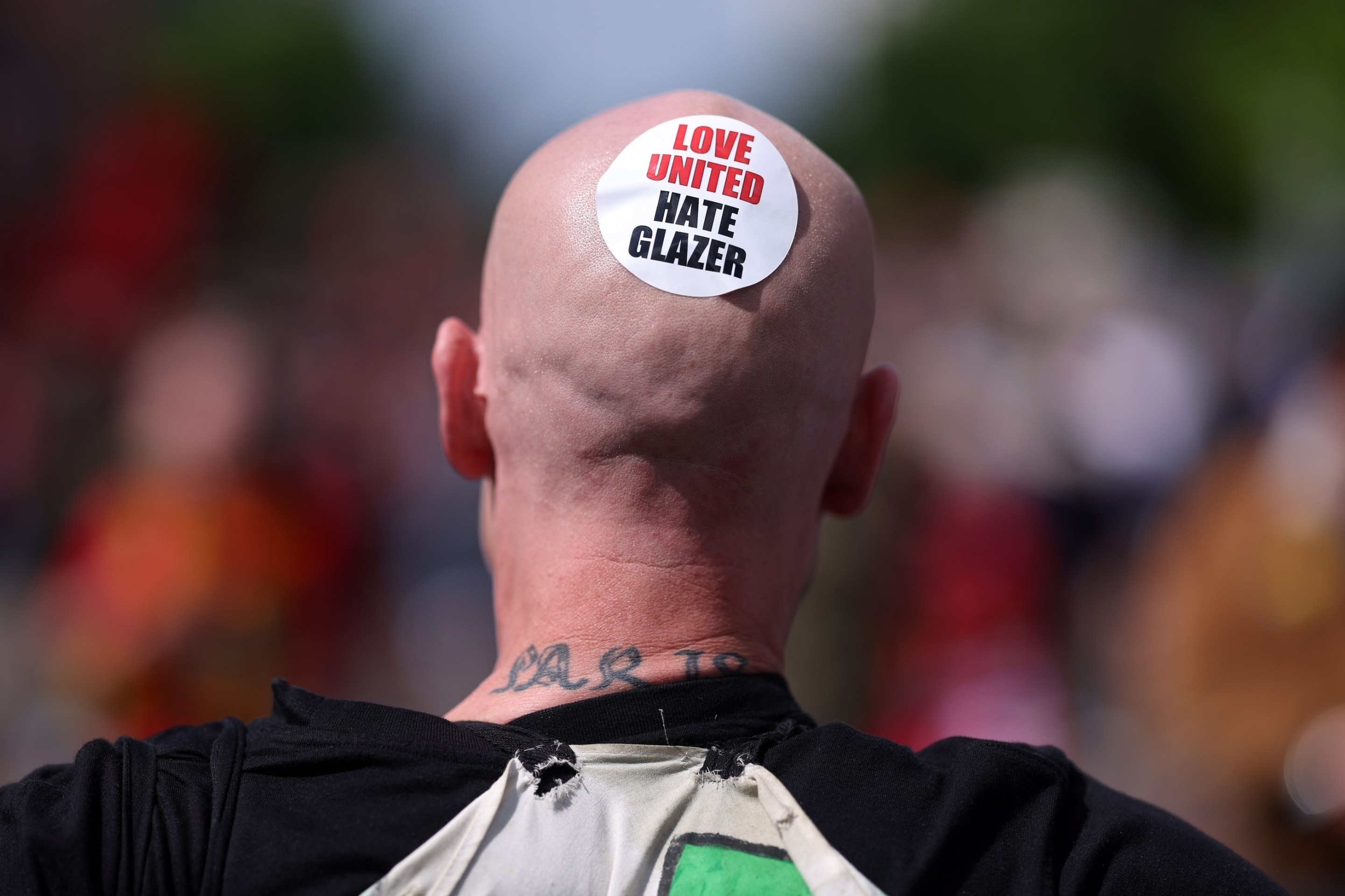 Fans of Manchester United protest against the club's owners outside the stadium, as a fan wears a sticker reading "Love United Hate Glazer" on his head.
