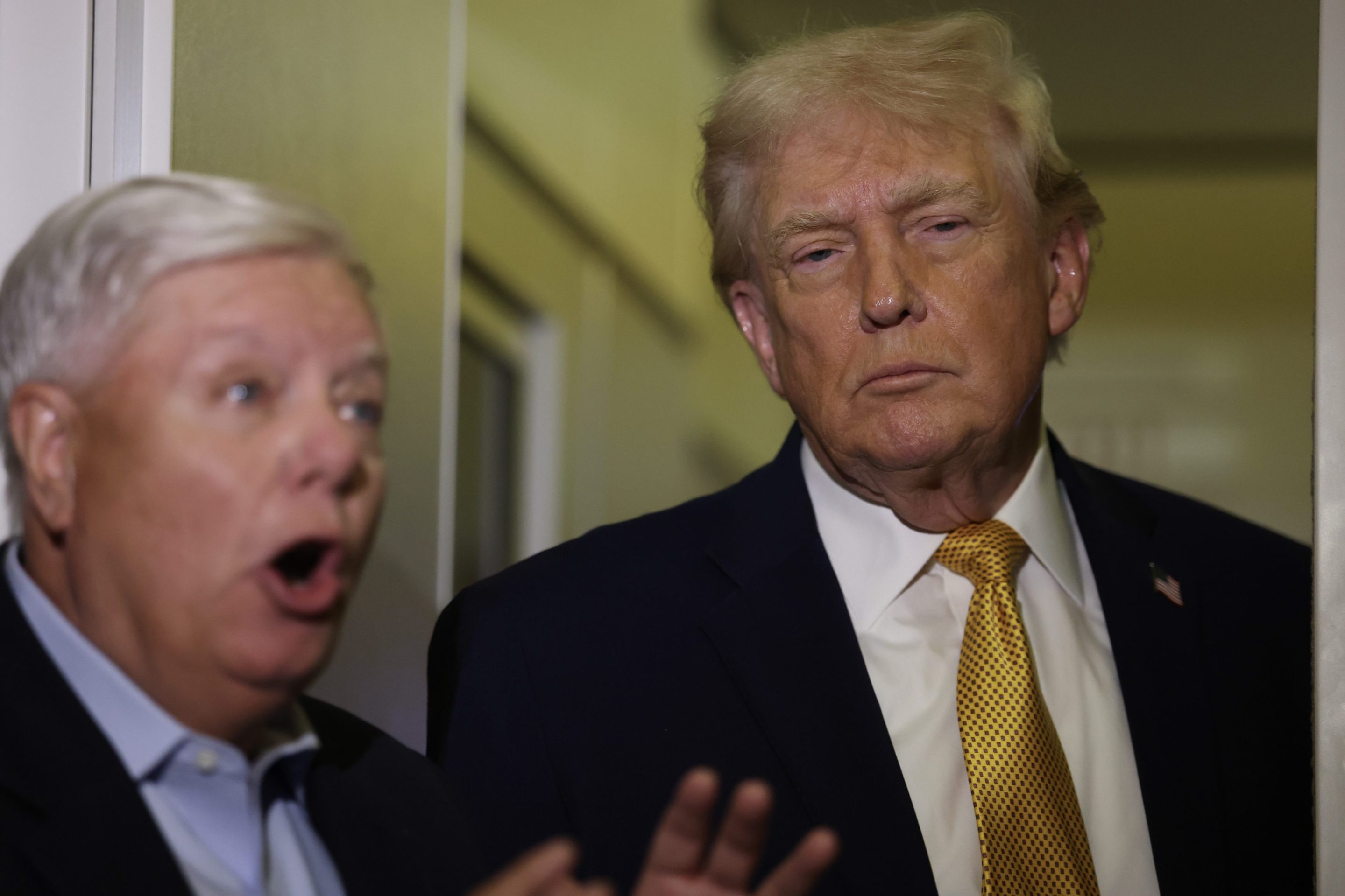 Donald Trump looks on as Lindsey Graham talks in the foreground.
