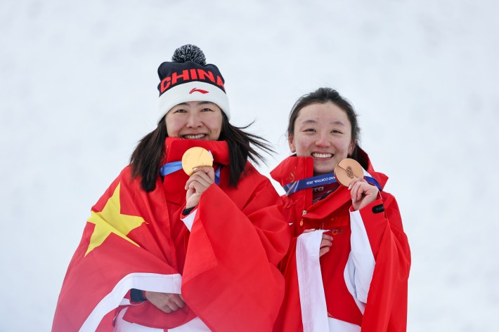 Gold medalist Mengtao Xu of Team People's Republic of China and Bronze medalist Qi Shao of Team People's Republic of China celebrate on the podium after the Women's Aerials Final on day twelve of the Milano Cortina 2026 Winter Olympic games