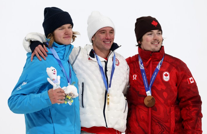 gold medalist Alex Ferreira of Team United States, Silver medalist Henry Sildaru of Team Estonia, and Bronze medalist Brendan MacKay of Team Canada celebrate on the podium after the Men's Freeski Halfpipe Final on day fourteen of the Milano Cortina 2026 Winter Olympic games