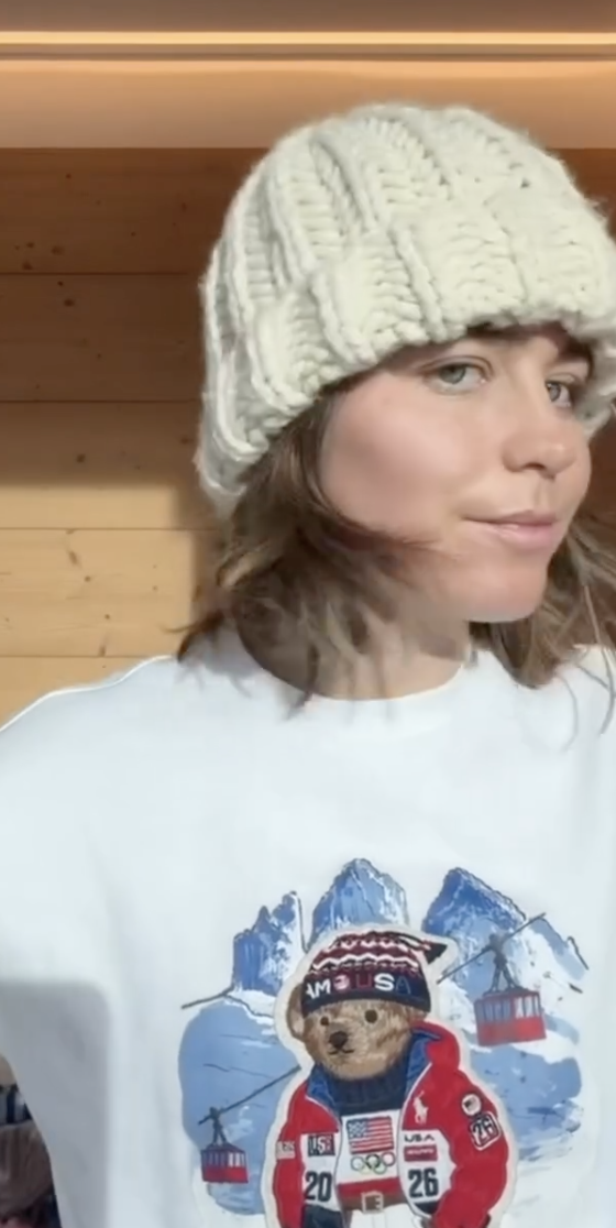 Maddie Mastro modeling one of her white beanies, and also a t-shirt with an Olympic bear on it, on Instagram.