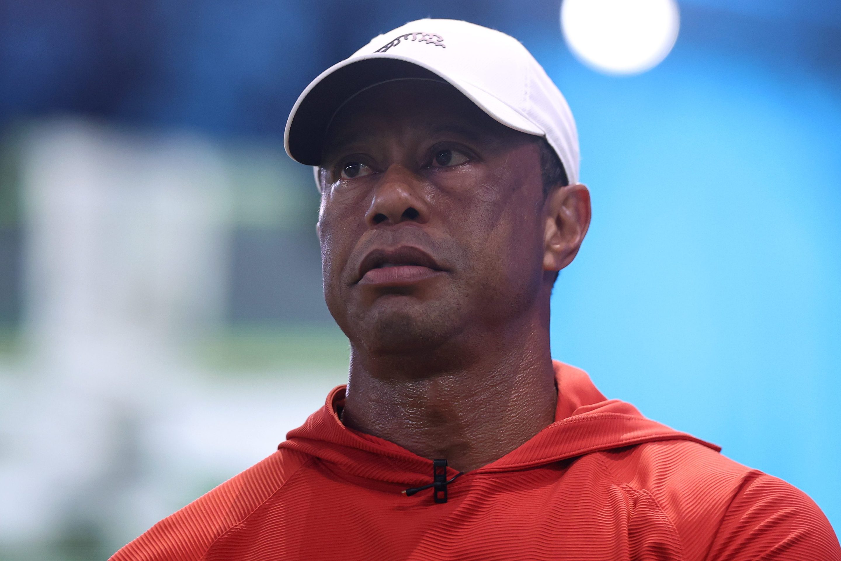 Tiger Woods of Jupiter Links Golf Club looks on before the match against the Los Angeles Golf Club at SoFi Center on March 23, 2026 in Palm Beach Gardens, Florida. He's wearing a red hoodie and a white baseball hat.