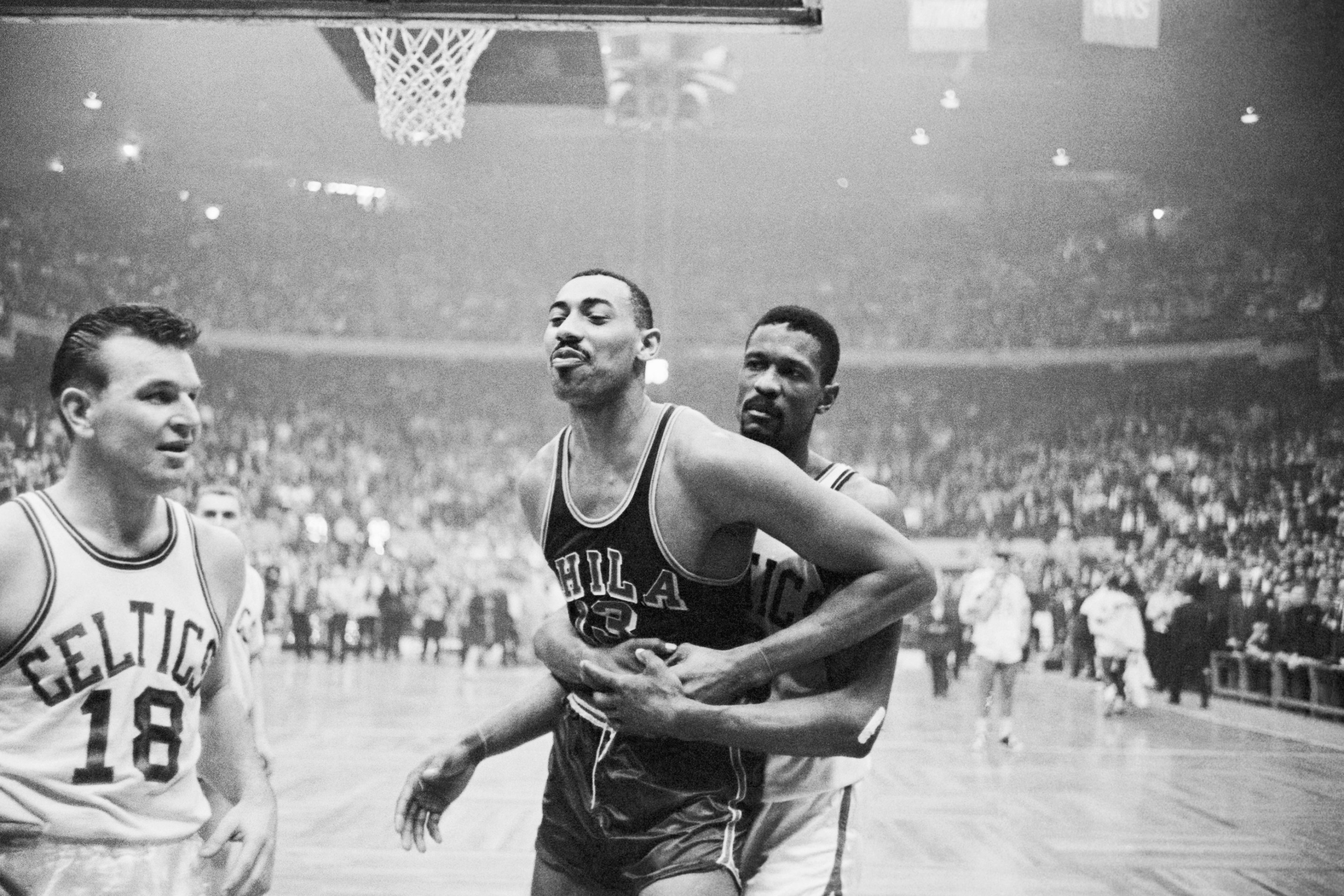 Celtics' Bill Russell (rear) pins Warriors' Wilt Chamberlain's right arm, and holds him, during wild 4th quarter in which both sides fought on April 1, 1962.