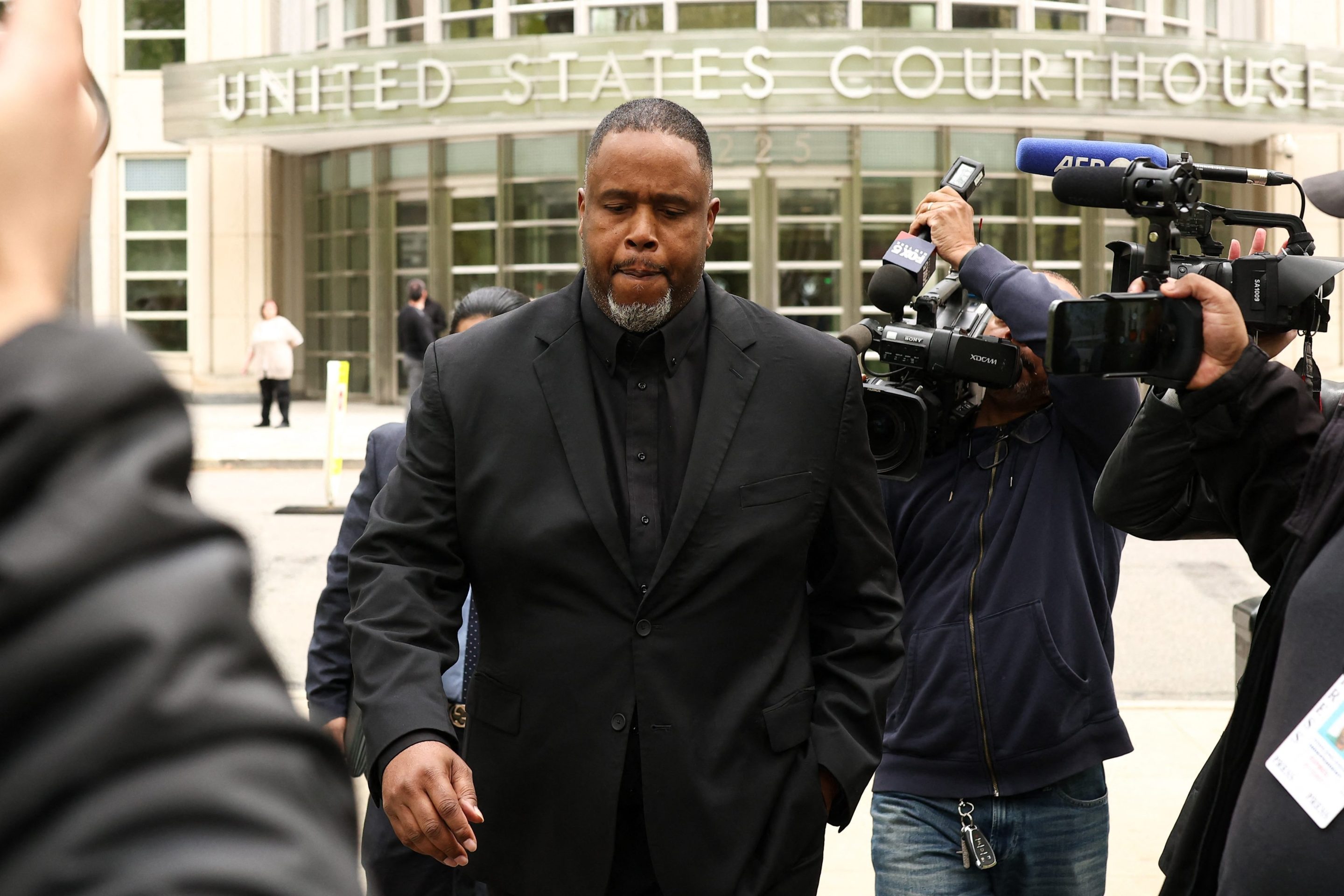 Former NBA player and assistant coach Damon Jones leaves the federal courthouse in Brooklyn, New York on April 28, 2026. He wore a black suit and has several news photographers around him.