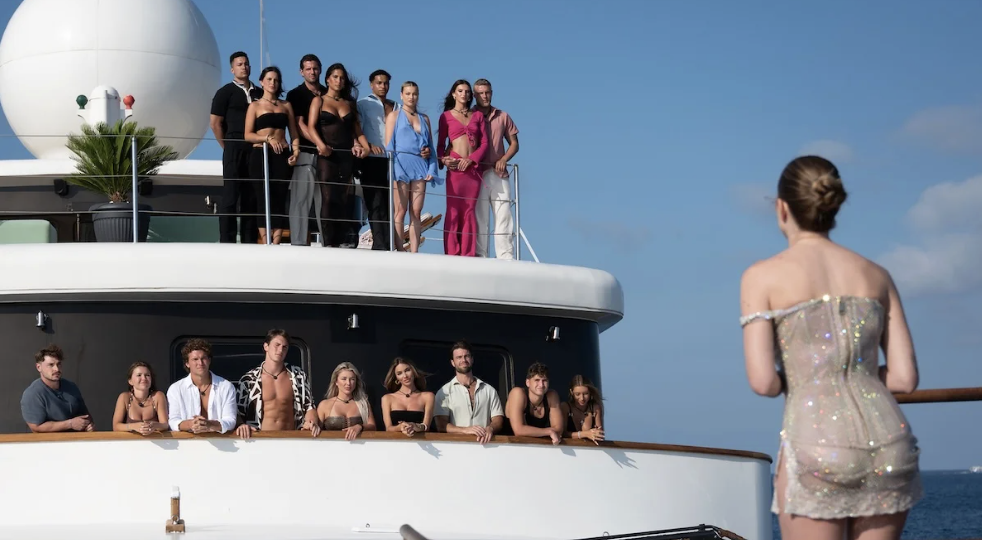 a woman stands on a plank while a bunch of hotties watch from the yacht