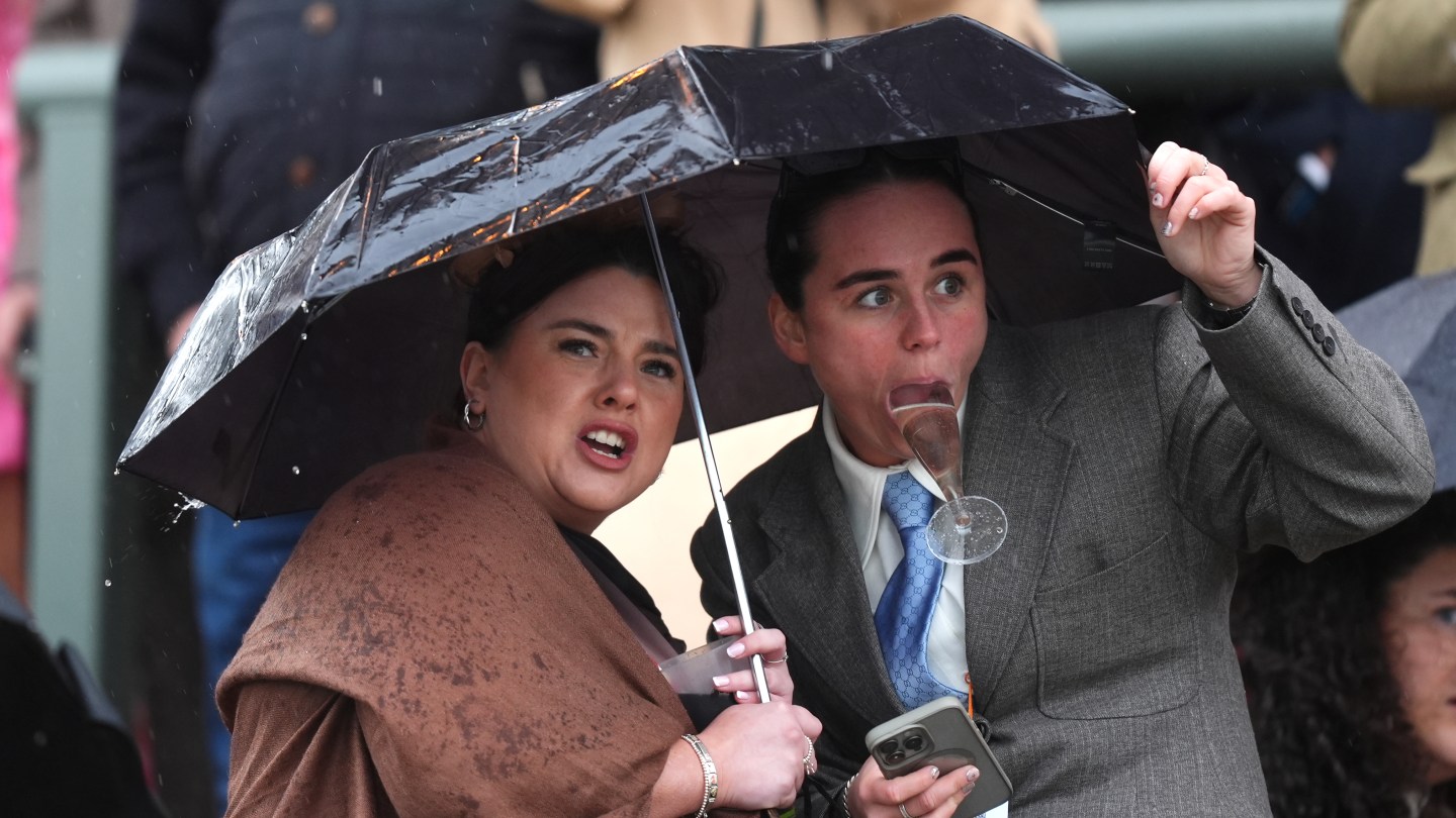 Racegoers attempts to protect themselves from the rain as they watch the Turners Mersey Novices' Hurdle on Grand National Day of the Randox Grand National Festival 2026 at Aintree Racecourse.