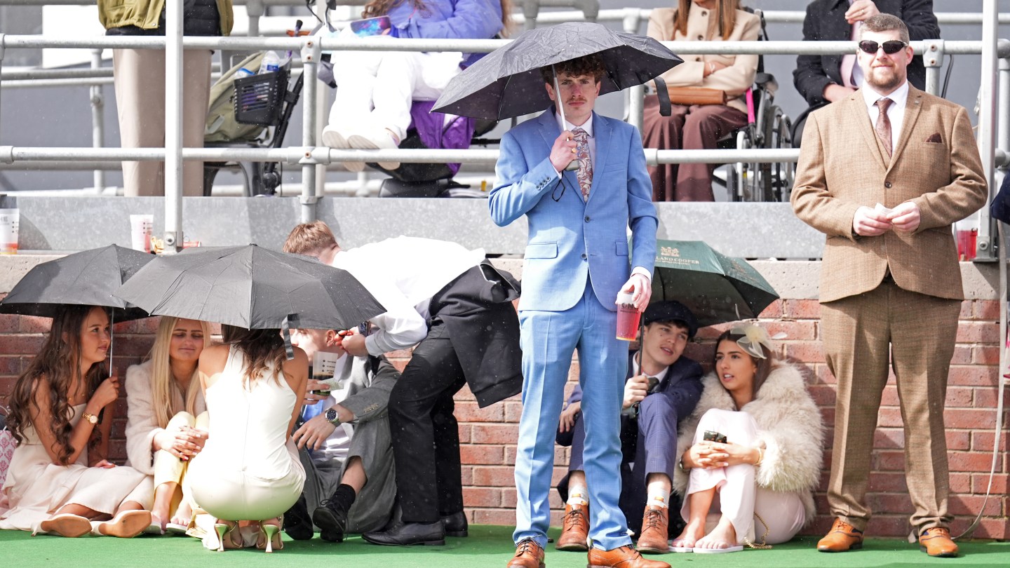 Racegoers shield themselves from the rain on Grand National Day of the Randox Grand National Festival 2026 at Aintree Racecourse.