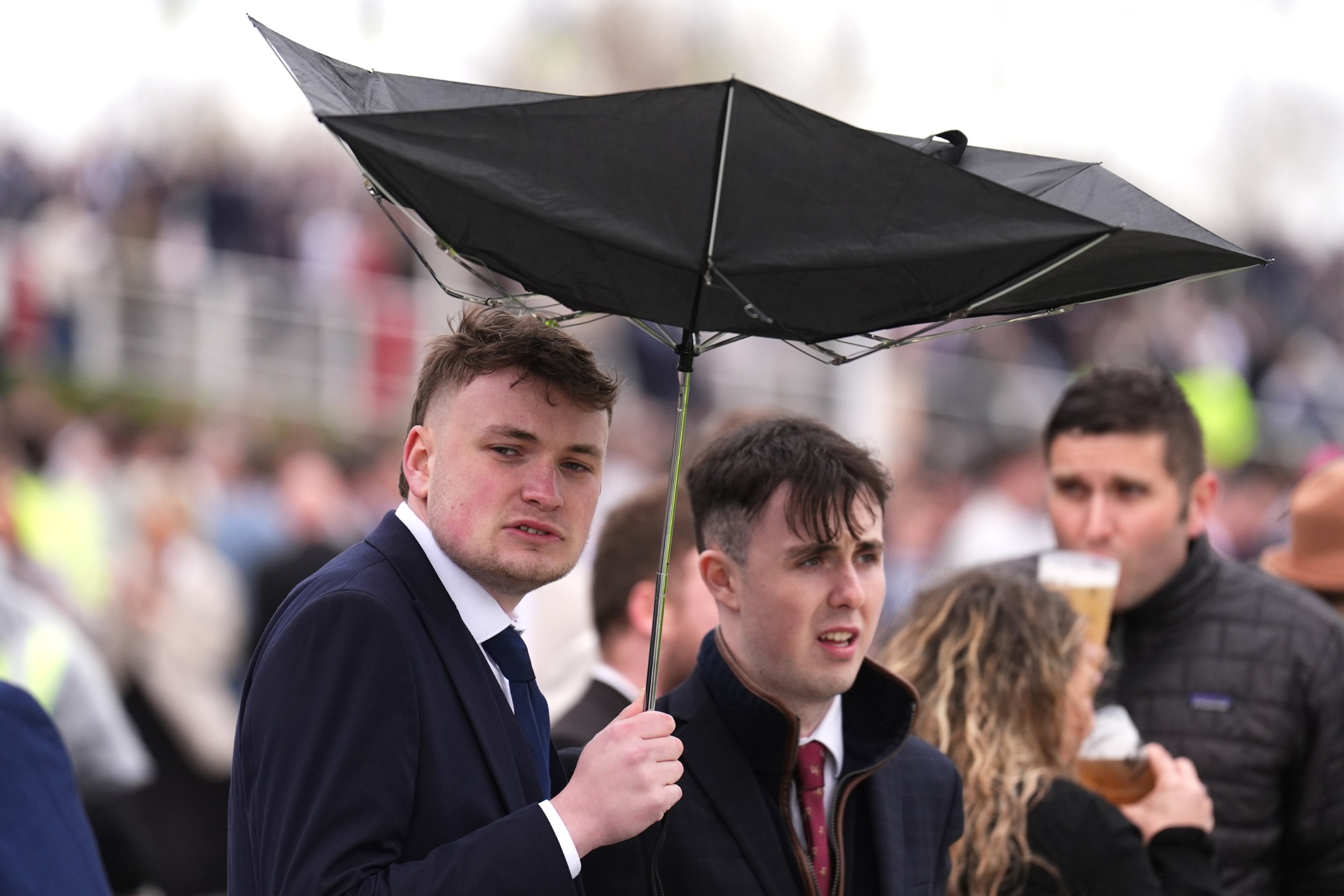 A racegoer holds an umbrella which is inside out on Grand National Day of the Randox Grand National Festival 2026 at Aintree Racecourse.