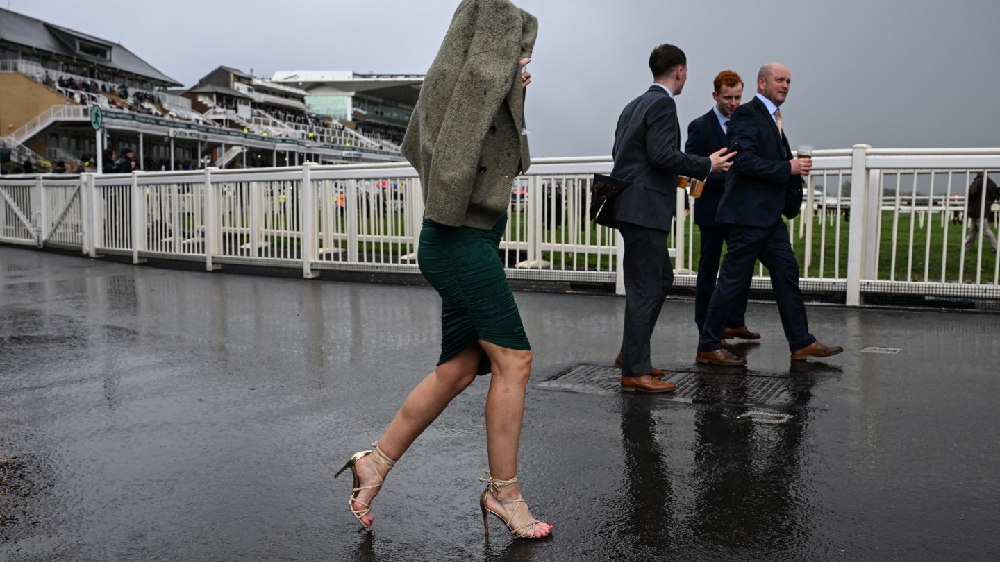 A racegoer (C) covers up to avoid the rain on the final day of the Grand National Festival horse race meeting at Aintree Racecourse.