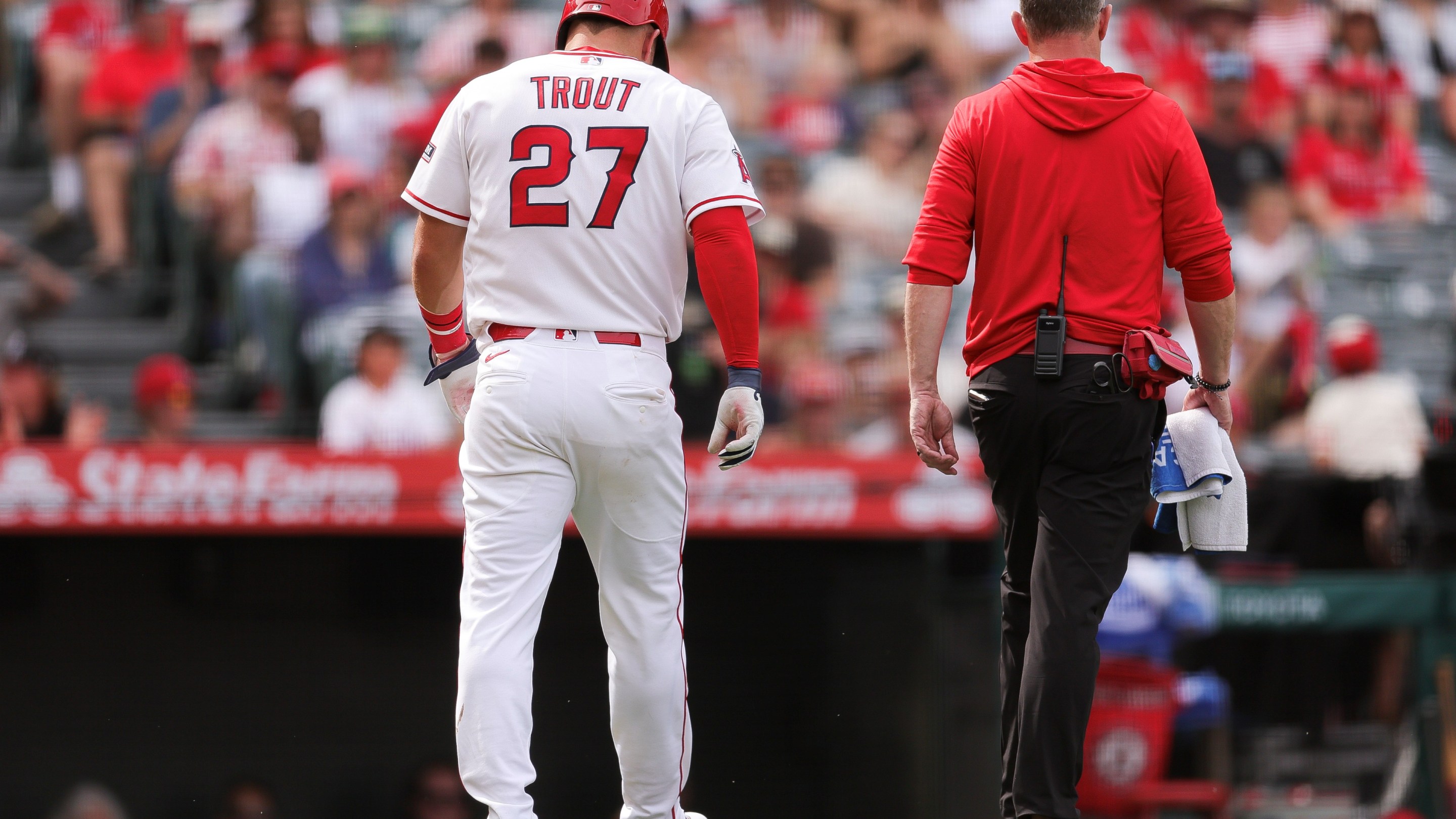 Mike Trout #27 of the Los Angeles Angels walks off the field with a trainer after being hit by a pitch.