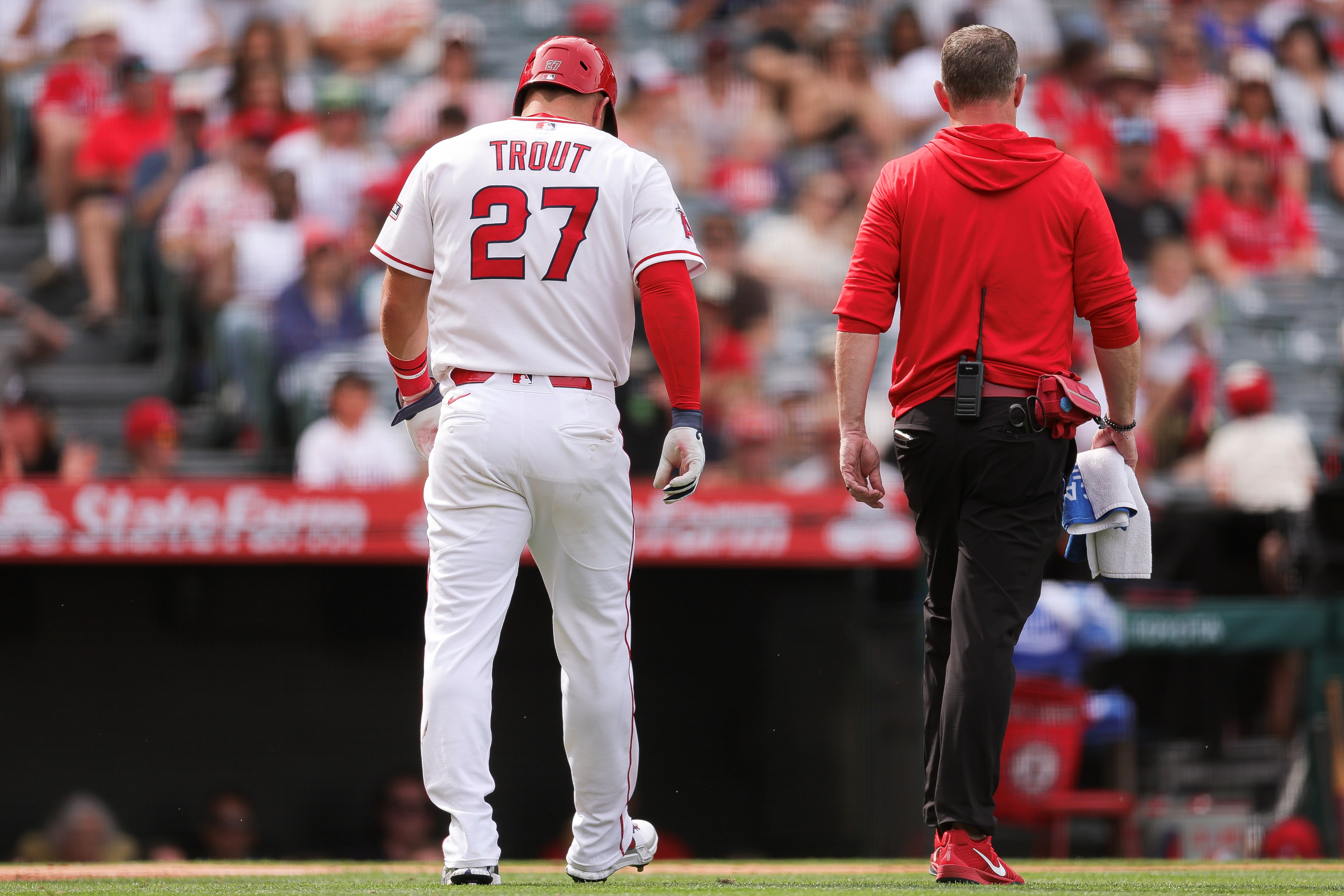 Mike Trout #27 of the Los Angeles Angels walks off the field with a trainer after being hit by a pitch.