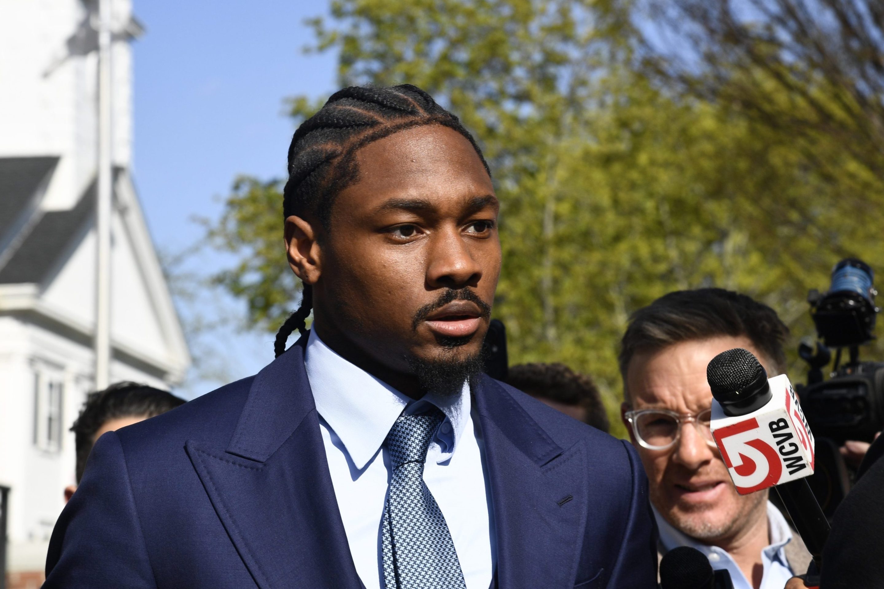 Professional football wide receiver Stefon Diggs walks out of Dedham District Court on May 4, 2026, following the first day of his assault trial. Diggs has pleaded not guilty to charges of felony strangulation and misdemeanor assault and battery. Diggs wore a suite and tie. Around him stood several news reporters.