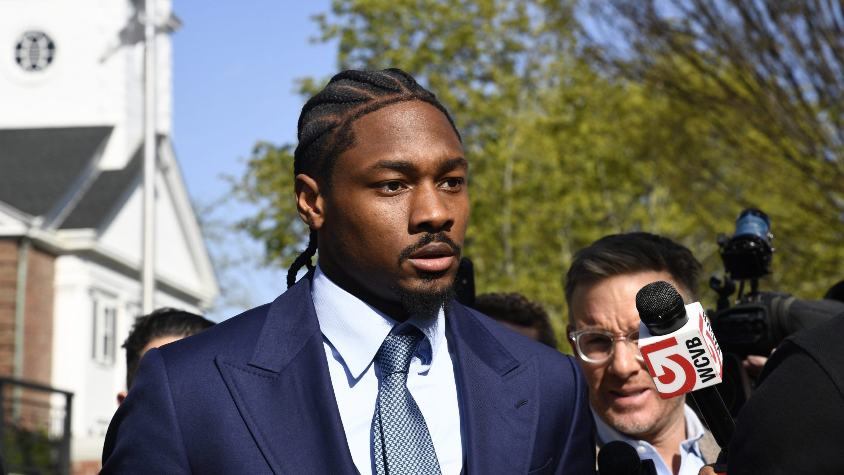Professional football wide receiver Stefon Diggs walks out of Dedham District Court on May 4, 2026, following the first day of his assault trial. Diggs has pleaded not guilty to charges of felony strangulation and misdemeanor assault and battery. Diggs wore a suite and tie. Around him stood several news reporters.