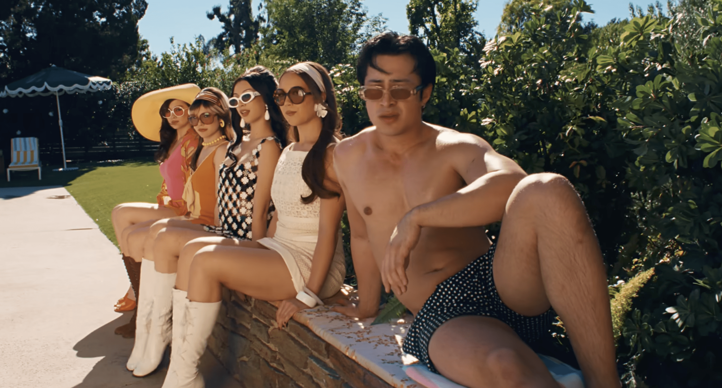 Hudson Williams, Alyssa Liu, Megan Skiendiel and Lola Tung sit side-by-side in the sun looking at the camera in Laufey's music video for "Madwoman"