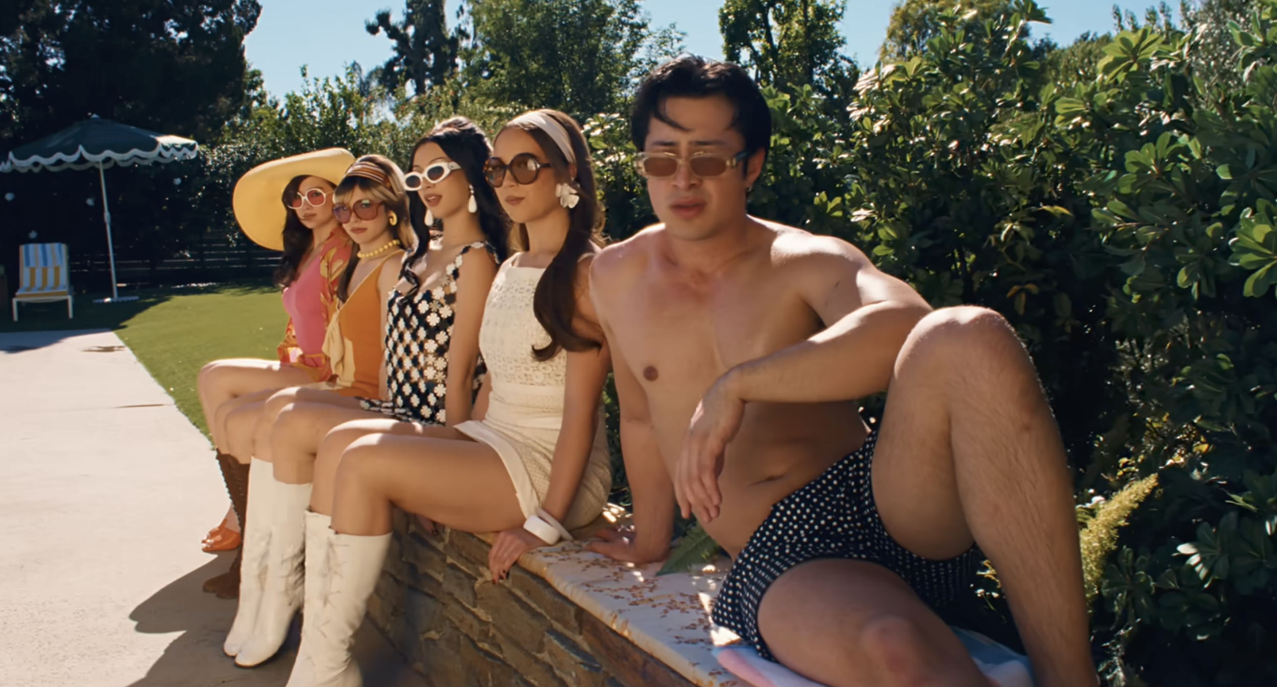 Hudson Williams, Alyssa Liu, Megan Skiendiel and Lola Tung sit side-by-side in the sun looking at the camera in Laufey's music video for "Madwoman"