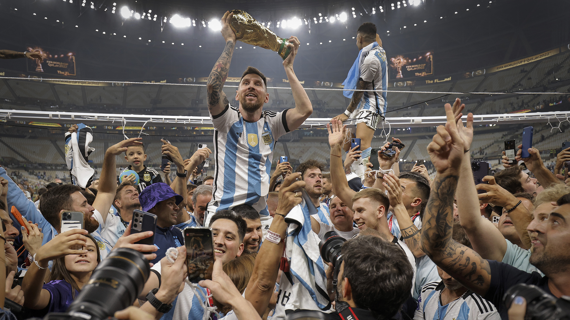 Lionel Messi of Argentina shows off the FIFA World Cup Trophy to fans while he is carried around the pitch on the shoulders of former teammate Sergio Aguero after the team's victory during the FIFA World Cup Qatar 2022 Final match between Argentina and France at Lusail Stadium on December 18, 2022 in Lusail City, Qatar.
